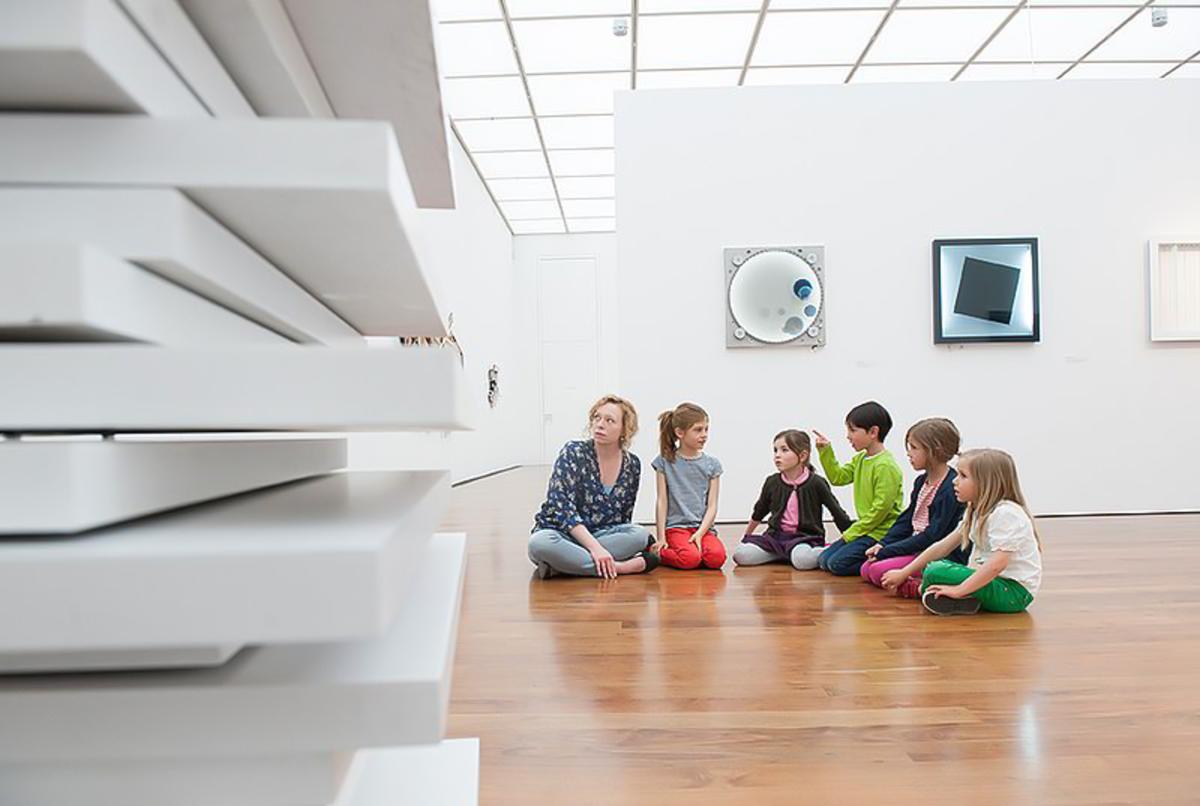 Kinder sitzen mit Pädagogin im Museum auf Holzfußboden